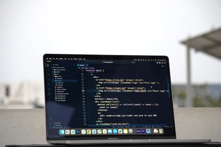 A MacBook Pro laptop displaying a code editor with a dark theme, showing lines of HTML, JavaScript, and React code on a bright outdoor surface. In the background, an overcast sky and blurred rooftops 